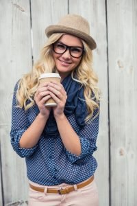 Happy trendy blonde holding coffee outdoors on wooden background