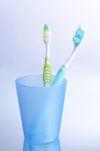 Toothbrushes in glass on light grey background