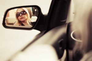 Blond fashion woman in sunglasses looking in the car mirror
